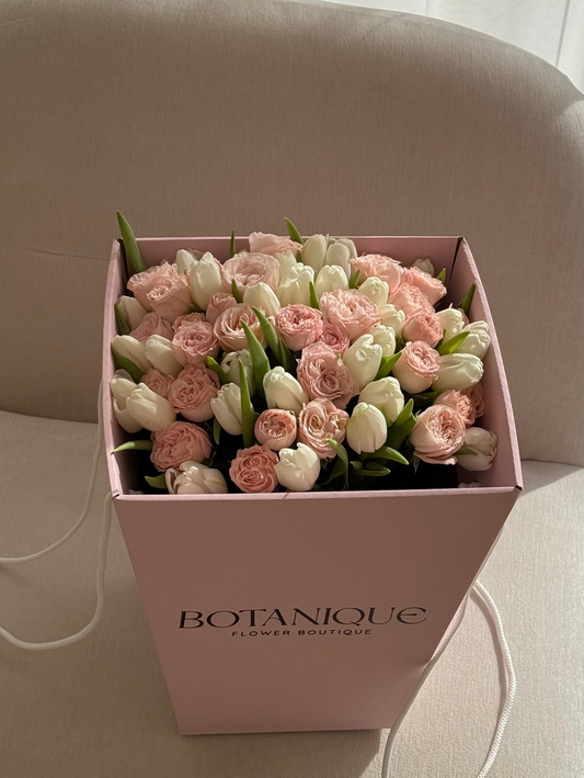 Pink box of flowers with 'BOTANIQUE' branding on a beige chair.