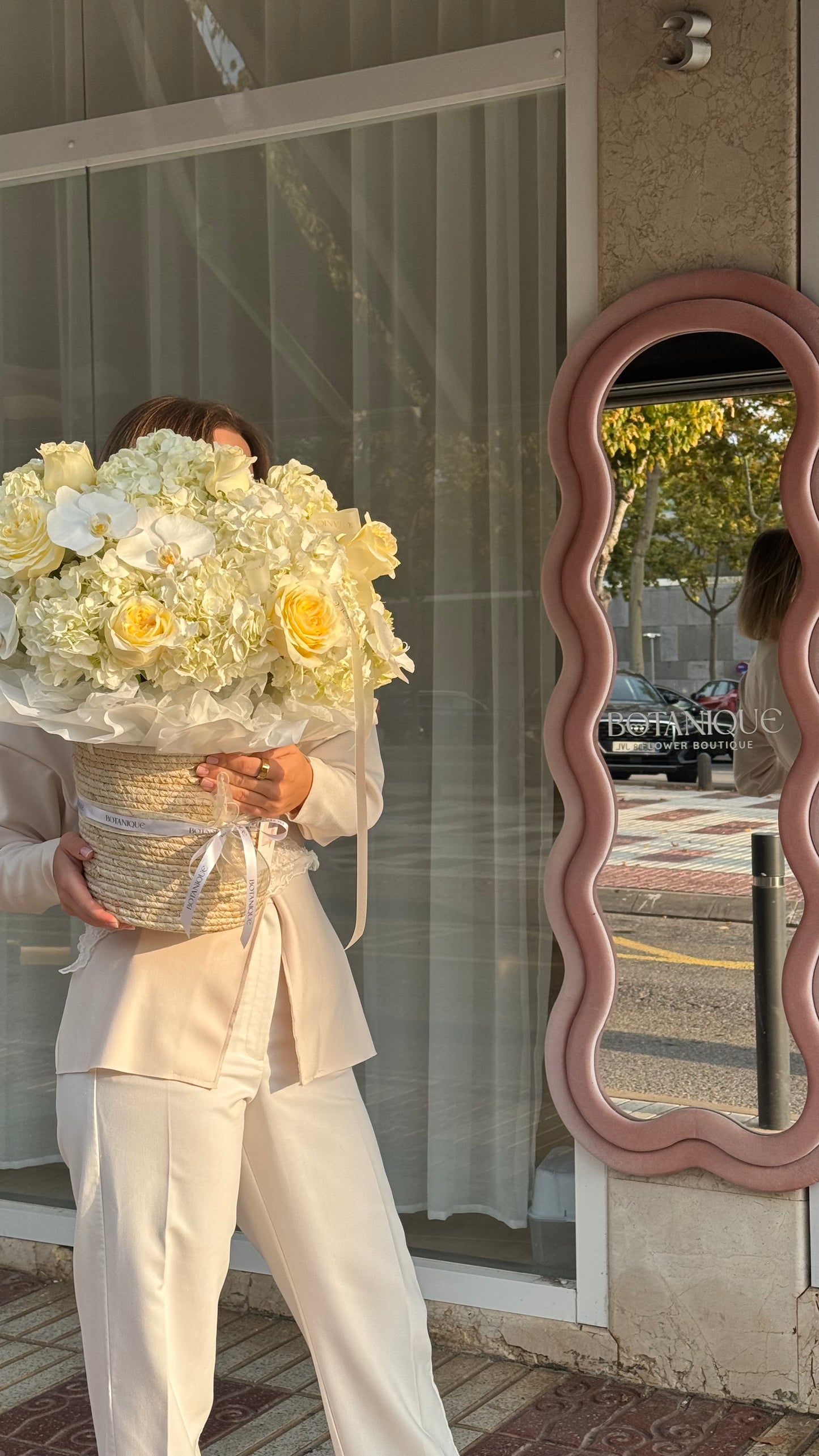 Person holding a large bouquet of flowers in front of a store window with a decorative mirror.