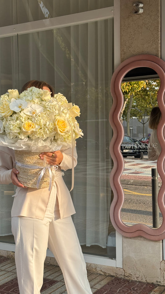 Person holding a large bouquet of flowers in front of a store window with a decorative mirror.